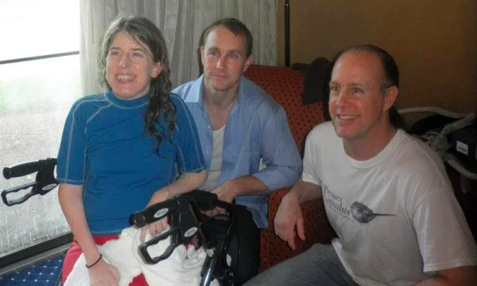 Family of three young people. A daughter in a blue shirt  sitting on a walker. Two brothers crouching near her